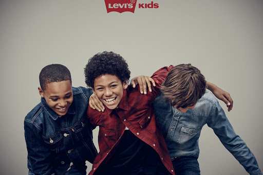 Three smiling boys embrace, wearing denim and plaid shirts in a studio shot, under a Levi's Kids logo, conveying friendship and youthful fashion.