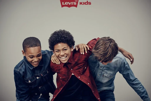 Three smiling boys embrace, wearing denim and plaid shirts in a studio shot, under a Levi's Kids logo, conveying friendship and youthful fashion.