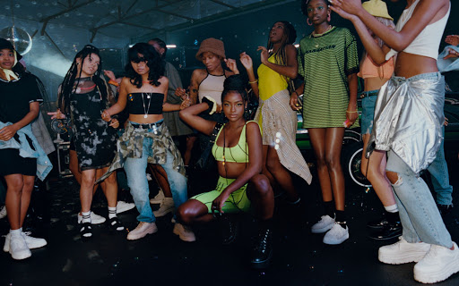 Group of diverse young adults dance in an indoor club environment with a disco ball, wearing streetwear and trendy casual clothing.