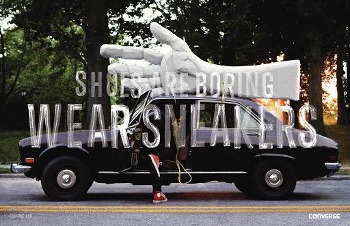 Vintage black car with an open door on a street, large text overlay, and a giant hand sculpture on top near trees.