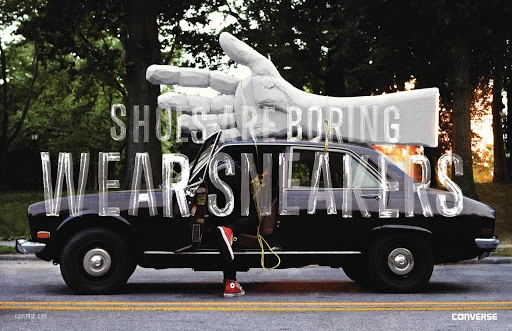 Vintage black car with an open door on a street, large text overlay, and a giant hand sculpture on top near trees.