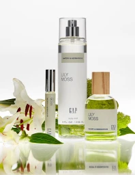 Three Gap Lily Moss fragrance bottles arranged with fresh white lily flowers and green foliage on a reflective white surface