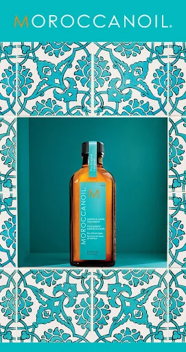 Moroccanoil bottle on a shelf against teal background and decorative tile border featuring floral patterns, showcasing hair care products.