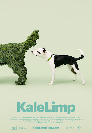 A black and white dog gazes at a dog-shaped kale sculpture in a studio setting, against a light green background. Text reads 'KaleLimp'.