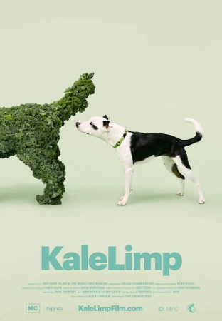 A black and white dog gazes at a dog-shaped kale sculpture in a studio setting, against a light green background. Text reads 'KaleLimp'.