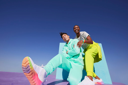 Two diverse adults in bright athletic wear pose on a geometric platform against a blue sky, showcasing a dynamic fitness lifestyle.