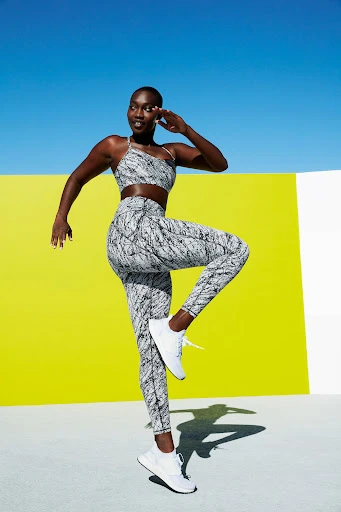 Athletic African-American woman in sportswear poses against a vibrant backdrop of blue, yellow, and white during daytime.