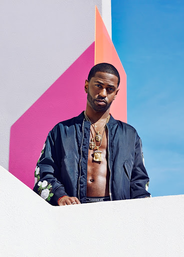 Portrait of Big Sean wearing a jacket with floral embroidery and gold necklaces against a geometric pastel wall and blue sky.