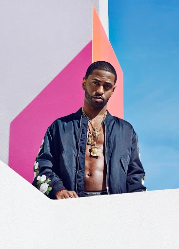 Portrait of Big Sean wearing a jacket with floral embroidery and gold necklaces against a geometric pastel wall and blue sky.