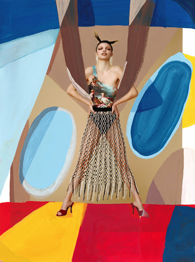 An adult woman strikes a pose against a colorful abstract backdrop, wearing a one-shoulder printed top and fringed see-through skirt, heels.
