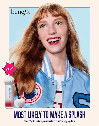 Benefit Cosmetics advertisement featuring a smiling woman with red hair wearing a blue jacket, and makeup product on a pink background.
