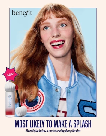 Benefit Cosmetics advertisement featuring a smiling woman with red hair wearing a blue jacket, and makeup product on a pink background.