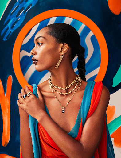 Portrait of a woman in profile wearing gold jewelry against a colorful abstract background with blue, orange, and white patterns.