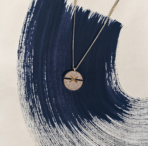 Elegant gold necklace with a round, sparkling pendant rests against a textured blue and white backdrop, showcasing jewelry.