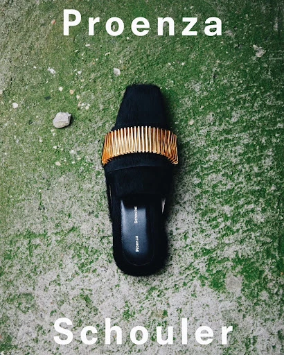 Black leather mule by Proenza Schouler, accessorized with a gold metallic band, displayed against a weathered concrete surface.