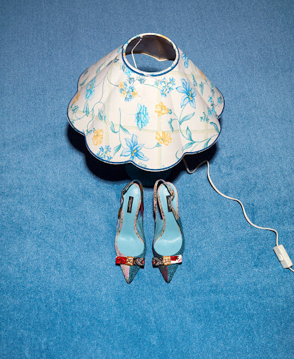 Overhead shot of floral lampshade and pointed-toe heels with bows on blue textured background in studio lighting.