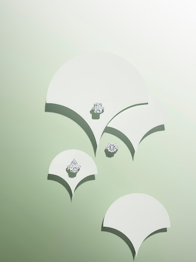High angle shot of four diamond rings on different sized white paper shapes with curved edges against a gradient green background.