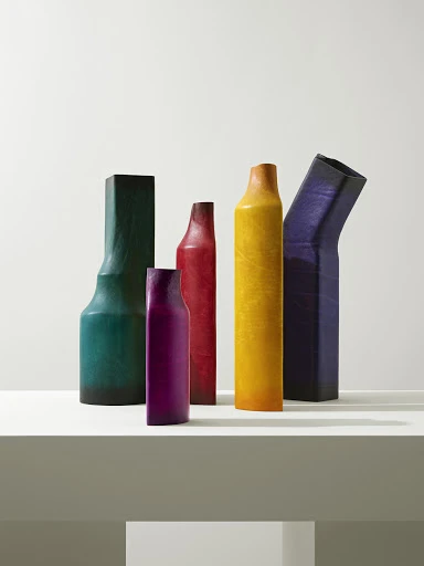 Still life shot of a collection of five assorted, colorful, textured vases on a light surface with a bright, neutral background.
