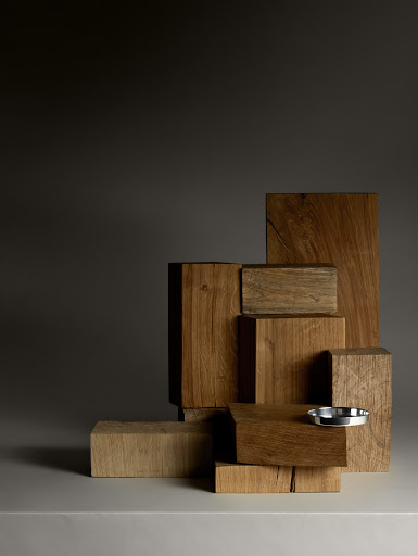 Stack of wooden blocks in varying sizes and shapes on a white surface with a small shiny metal bowl.  Brown and gray tones.