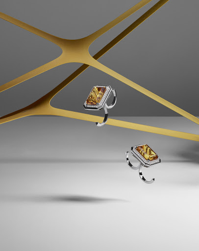 Two rings with orange gemstones are displayed on gold bars against a gray backdrop in this jewelry product still-life photograph.