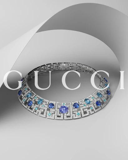 Close-up of a striking silver-tone Gucci choker necklace adorned with blue and clear gemstones, displayed on a light grey background.