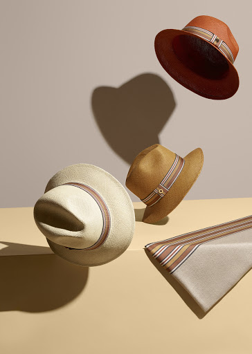 Still life composition of floating straw hats in tan, brown, and beige tones on a pale background. Millinery fashion photography.