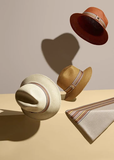 Still life composition of floating straw hats in tan, brown, and beige tones on a pale background. Millinery fashion photography.