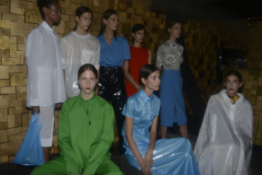 Runway show featuring a diverse group of fashion models showcasing shiny and colorful garments on a set with a textured gold wall.