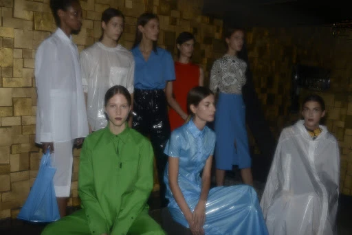 Runway show featuring a diverse group of fashion models showcasing shiny and colorful garments on a set with a textured gold wall.