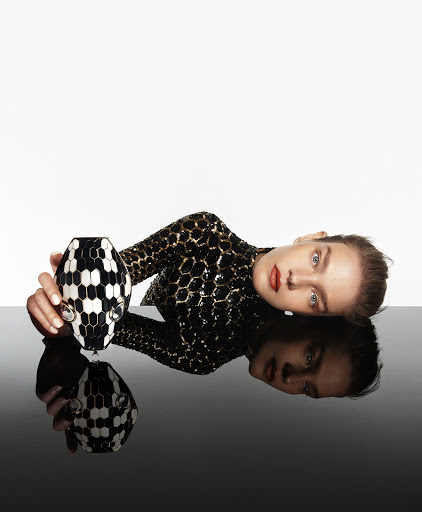 Woman in sequin top poses with a black and white patterned vase against a stark white and black reflective surface.