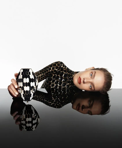 Woman in sequin top poses with a black and white patterned vase against a stark white and black reflective surface.
