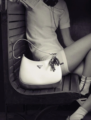 Monochrome shot of a woman on a bench with a Prada handbag and keys, emphasizing fashion and urban lifestyle in a posed composition.