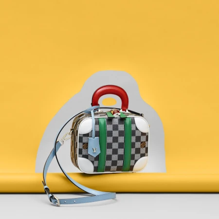 Multicolor designer handbag with a grey checkerboard pattern, red handle, green stripes, and blue shoulder strap on a yellow set.