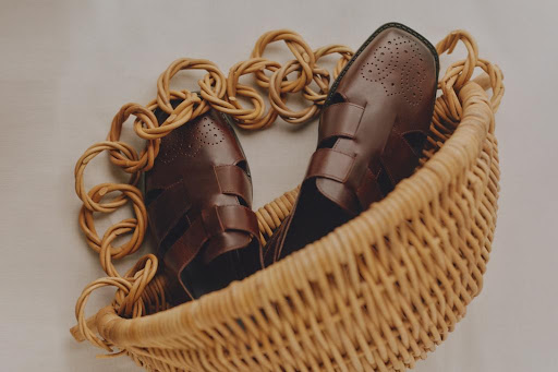 Dark brown leather fisherman sandals in a woven basket, showcasing detailed design and craftsmanship against a soft, neutral background.