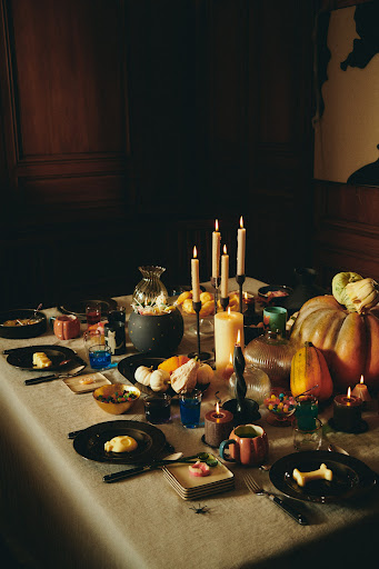 A table setting with pumpkins, candles, and dinnerware creates a festive ambiance, perfect for a seasonal gathering or Halloween feast.