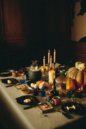 A table setting with pumpkins, candles, and dinnerware creates a festive ambiance, perfect for a seasonal gathering or Halloween feast.