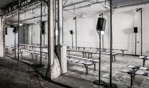 Empty fashion show venue with rows of benches, speaker system, and industrial architecture in monochrome tones, highlighting the set-up.