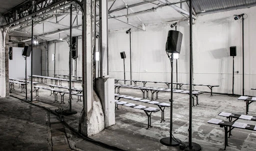 Empty fashion show venue with rows of benches, speaker system, and industrial architecture in monochrome tones, highlighting the set-up.
