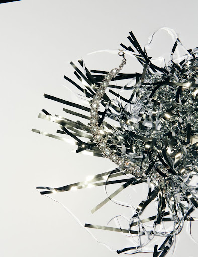 Close-up of a silver crystal necklace with silver tinsel on a white backdrop, showing texture, detail, and reflective qualities.