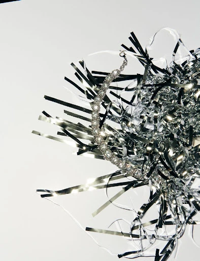 Close-up of a silver crystal necklace with silver tinsel on a white backdrop, showing texture, detail, and reflective qualities.