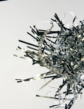 Close-up of a silver crystal necklace with silver tinsel on a white backdrop, showing texture, detail, and reflective qualities.