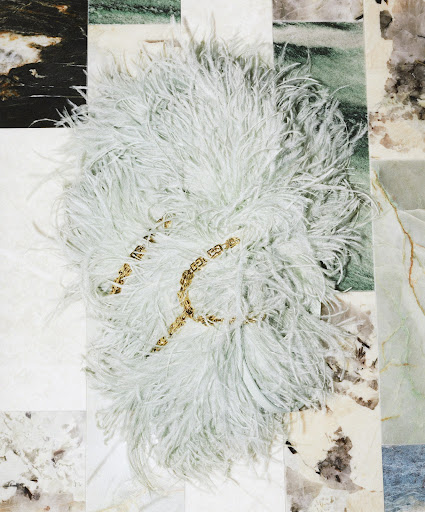 Elegant composition featuring a white feather boa with gold chain on a multi-toned marble tile background creating a luxurious aesthetic.