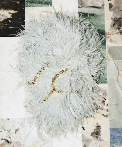 Elegant composition featuring a white feather boa with gold chain on a multi-toned marble tile background creating a luxurious aesthetic.