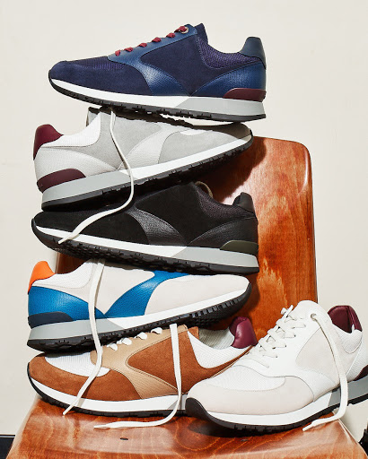 Stacked colorful running shoes on a wooden chair against a plain backdrop, showcasing a variety of athletic footwear in a studio setting.