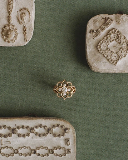Close-up of an ornate gold ring with diamonds, set against a muted green fabric background and surrounded by vintage molds.