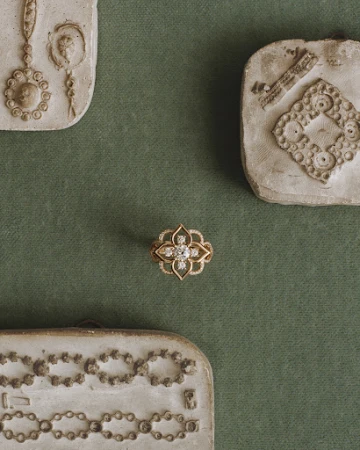 Close-up of an ornate gold ring with diamonds, set against a muted green fabric background and surrounded by vintage molds.