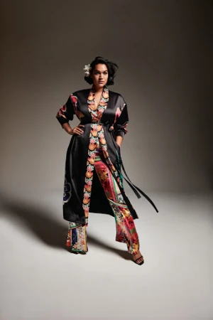 Model wearing a black silk robe and patterned trousers with floral prints standing against a grey seamless background.