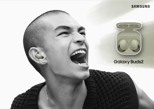 A person with short hair is seen wearing wireless earbuds, next to a pair of wireless earbuds in their charging case with Samsung logo.