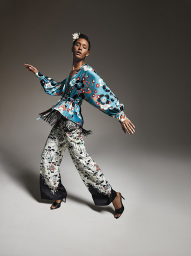 A woman in a stylish patterned outfit poses in motion, showcasing a modern take on fashion with a floral blouse and wide-leg pants.