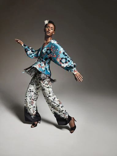 A woman in a stylish patterned outfit poses in motion, showcasing a modern take on fashion with a floral blouse and wide-leg pants.